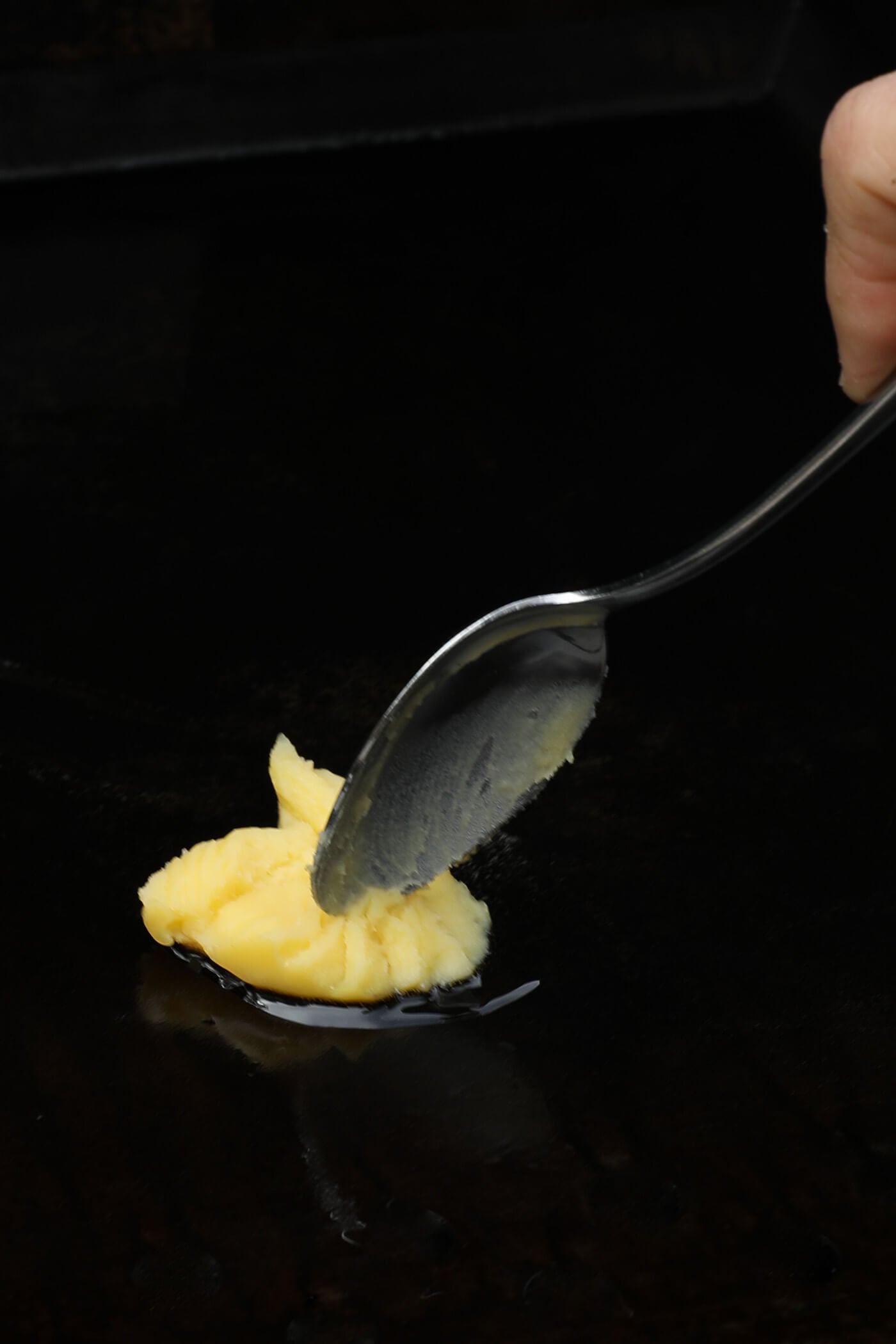 A hand using a spoon to spread butter or ghee on the griddle so it melts.