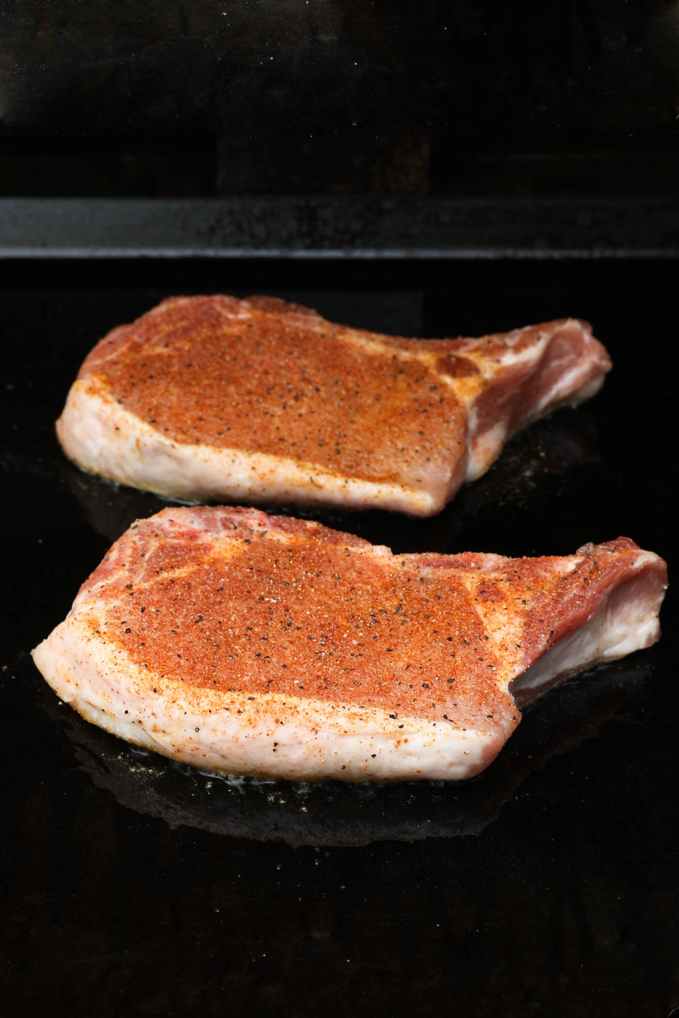 Two seasoned pork chops just placed on a griddle.