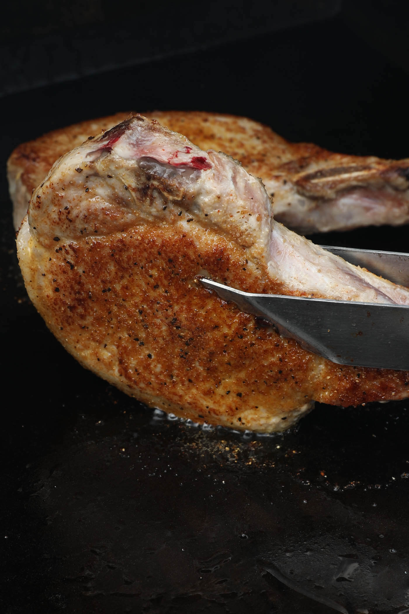 Using tongs to sear the edges of a pork chop on a griddle.