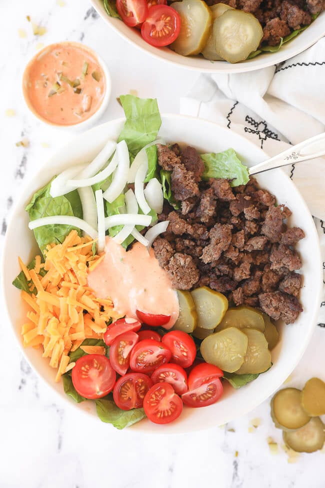 Big mac salad in a bowl with ground beef, cheese, tomato, pickle, onion and sauce in middle.