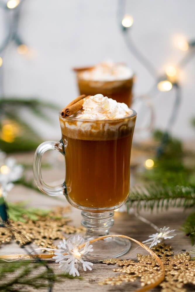 Hot buttered rum in a clear mug with whip cream and cinnamon sticks on top