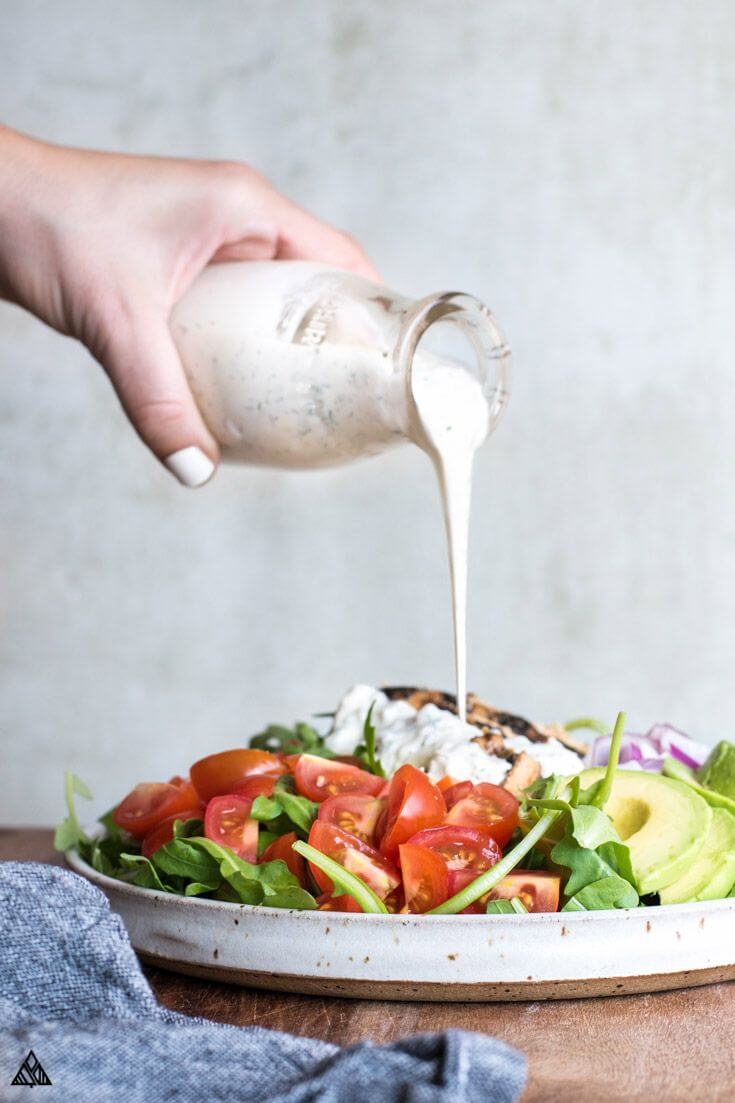 Straight on image of homemade ranch pouring onto a plate of salad with tomato chicken and avocado