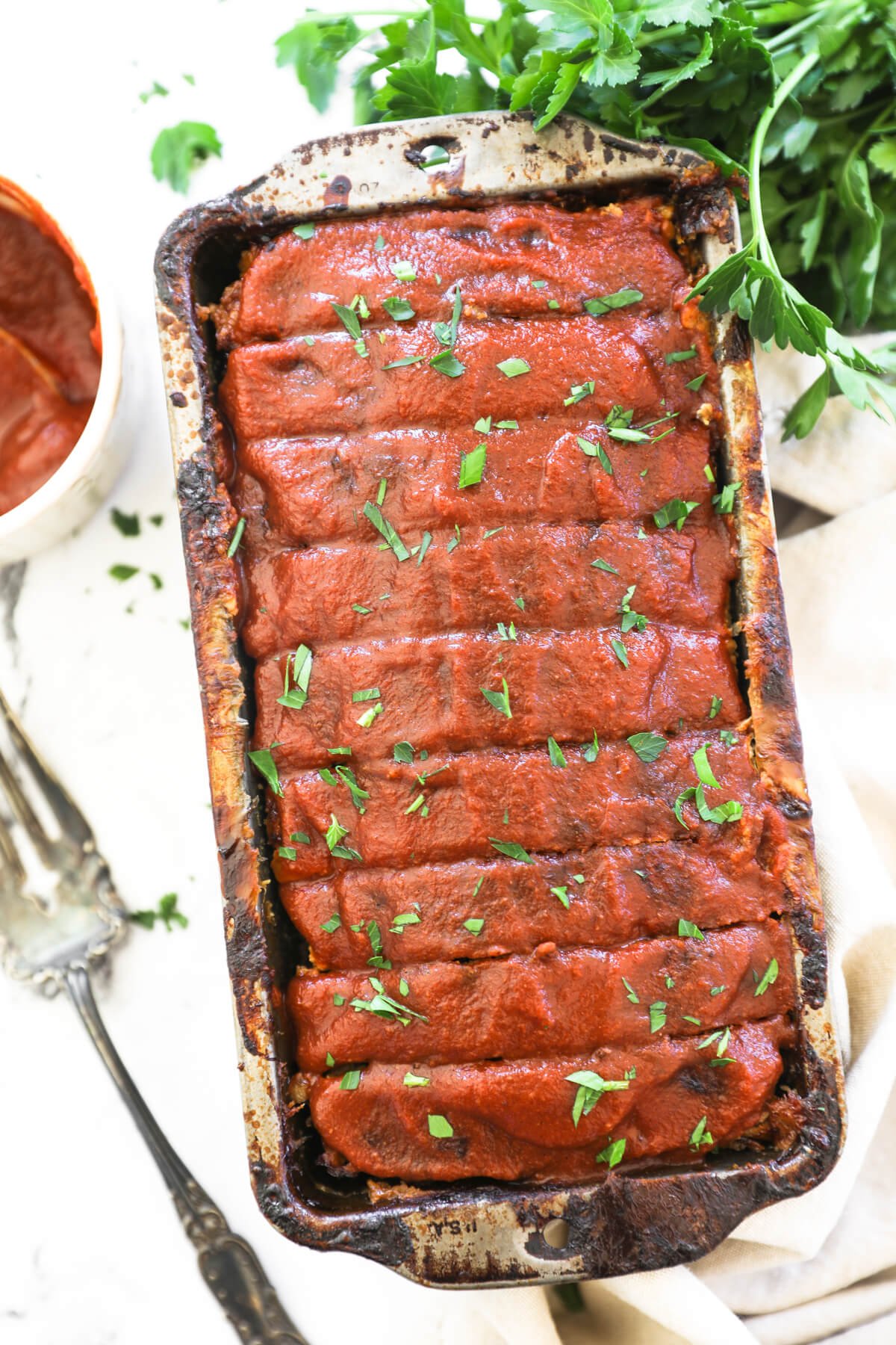 Overhead image of a loaf pan with meatloaf sliced in it. Topped with a ketchup glaze and chopped parsley.
