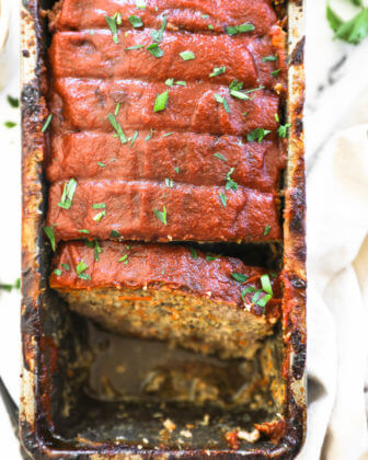 Overhead image of meatloaf in a loaf plan sliced and a couple pieces removed from the pan. The meatloaf is topped with paleo ketchup and chopped parsley.