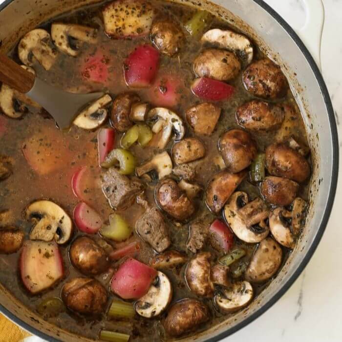 Overhead shot of keto beef stew in a dutch oven with mushrooms, celery and radishes