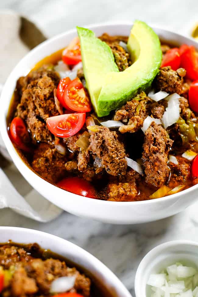 Angled shot of keto chili in a bowl with chopped onion, tomatoes and avocado. 