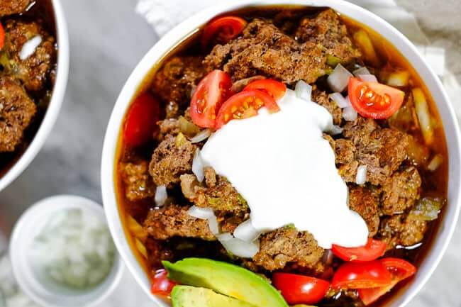 Keto chili served in bowls and topped with chopped onion, tomatoes, avocado and coconut yogurt. 