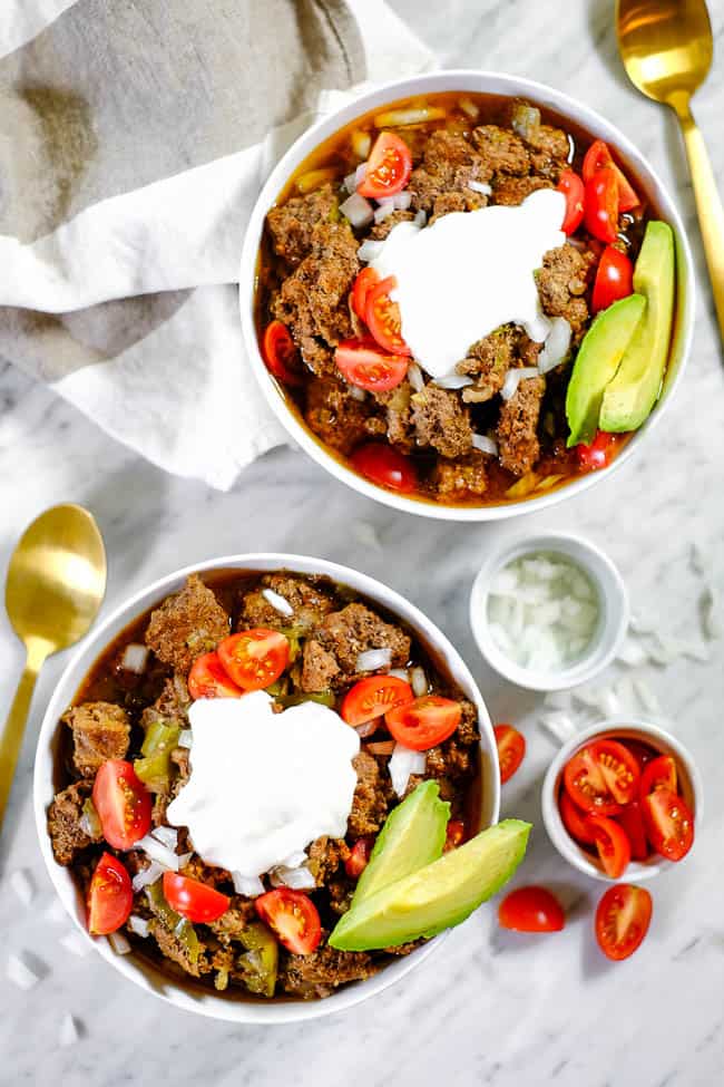 Pulled out shot of keto chili in bowls topped with chopped onion, tomatoes, avocado and coconut yogurt. 