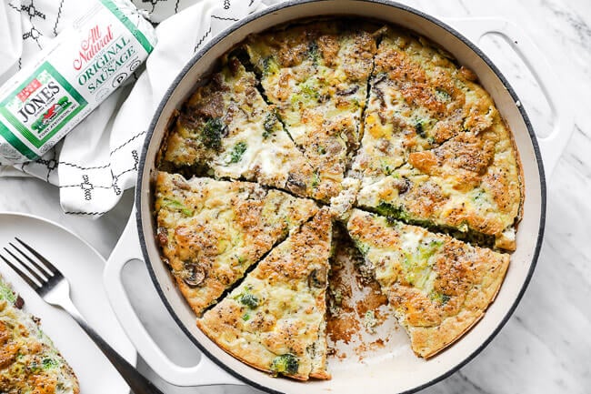 Horizontal overhead image of keto frittata in a large skillet, cut into slices like a pie with one piece removed from pan. 