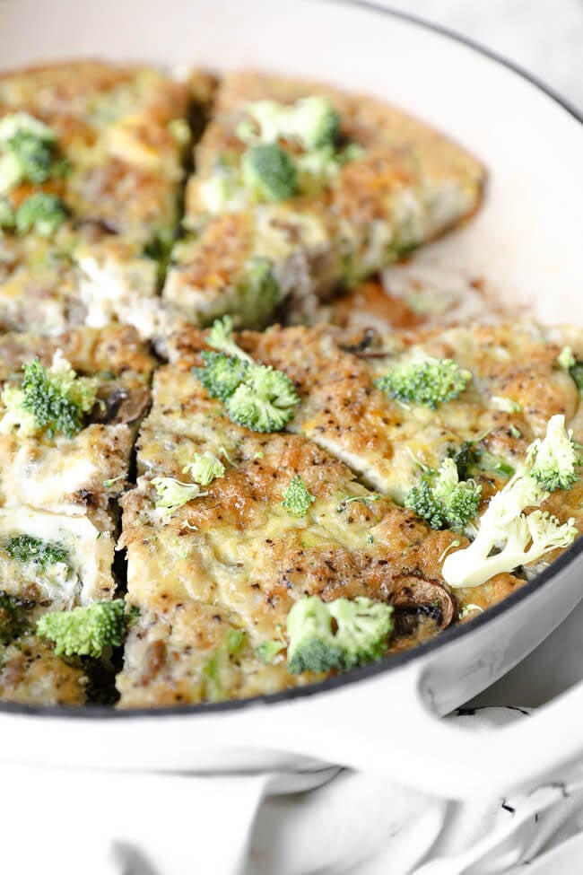Vertical angled close up shot of Keto frittata in skillet with extra broccoli bits sprinkled on top. 