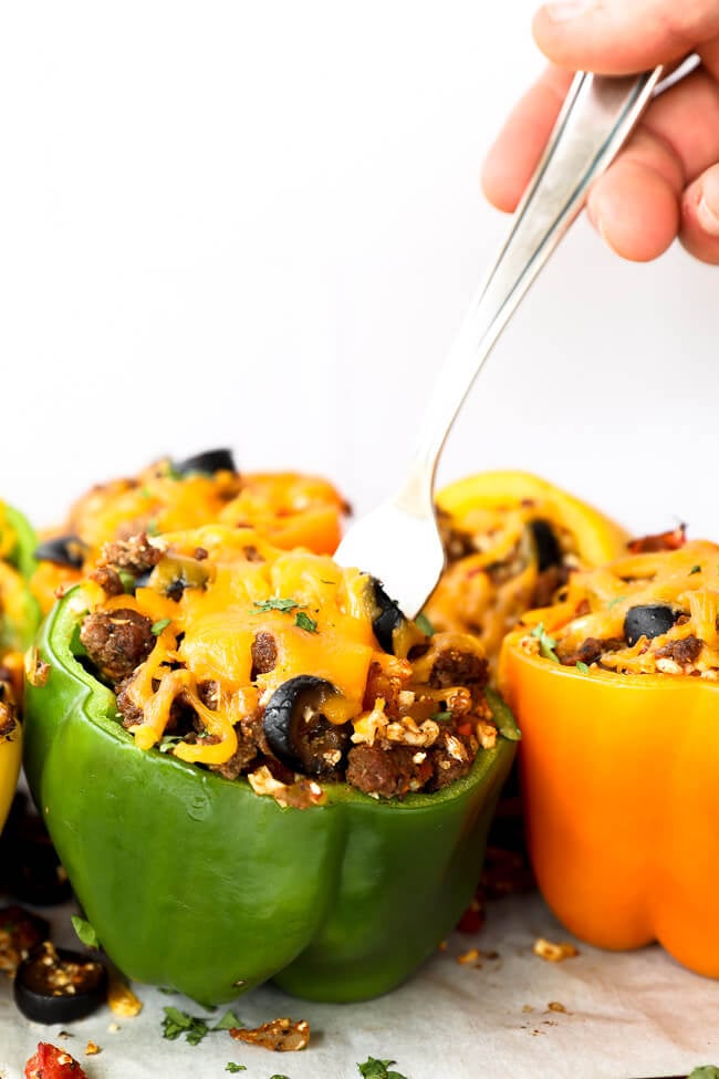 Taco stuffed bell peppers topped with cheese. Hand and fork going into one pepper.