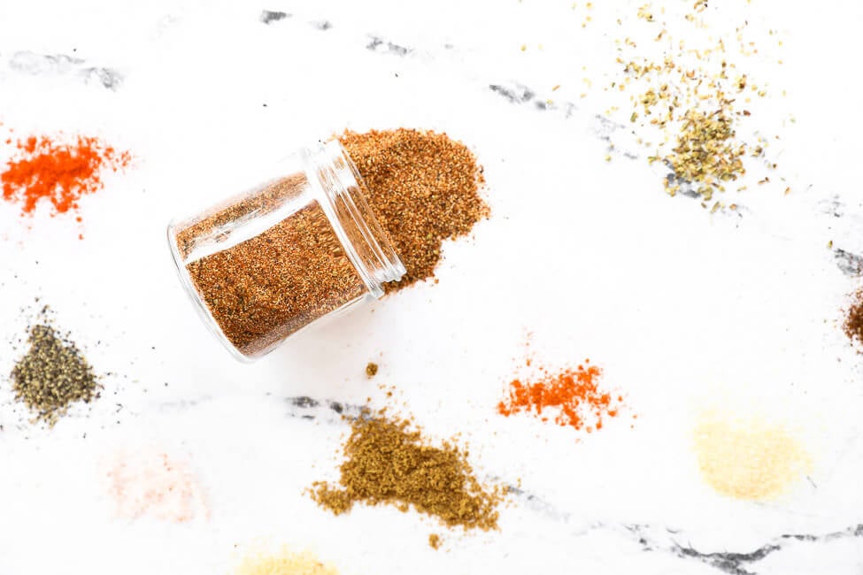 various seasonings scattered on a countertop with a small jar in middle