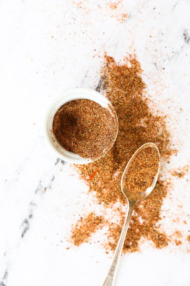 Taco seasoning in a ramekin with seasoning spilled out and spoon