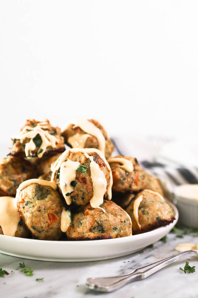 Image verticale d'une pile de boulettes de viande céto sur une assiette avec de la sauce aïoli épicée arrosée sur le dessus et en cascade sur les côtés des boulettes de viande. 