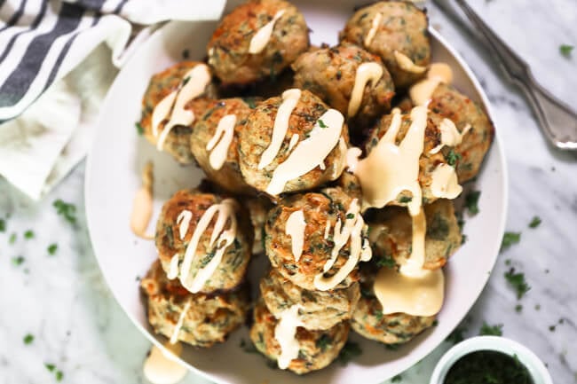 Horisontalt overheadbillede af keto kalkunfrikadeller stablet op på en tallerken med krydret aioli-sauce drysset ud over det hele. 