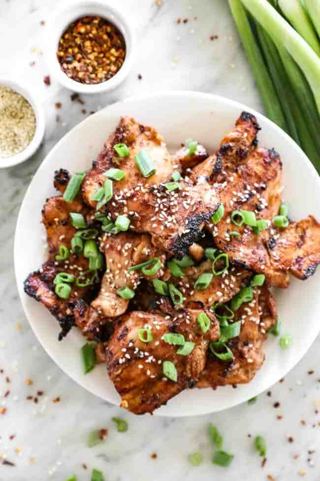 Overhead shot of korean bbq chicken stacked on a plate with sliced green onions on top