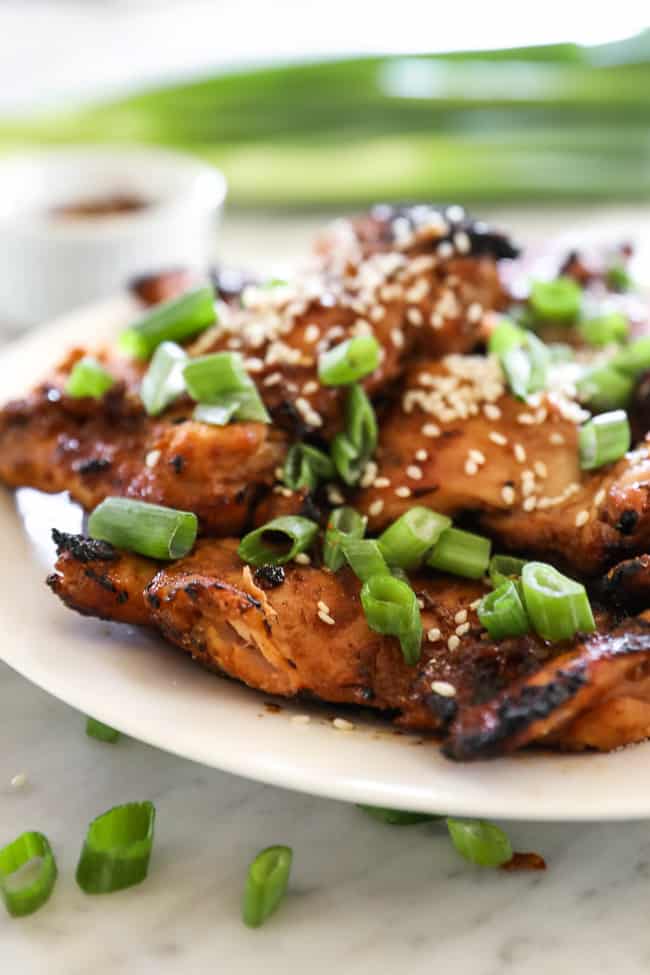 Angle shot of korean bbq chicken stacked on a plate with green onion slices on top