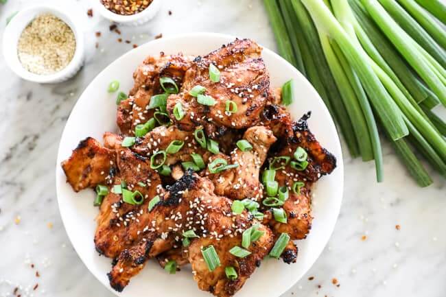 Korean BBQ chicken on a plate with green onions to the right horizontal image