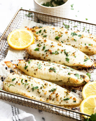 Angled image of air fryer tilapia in cooking basket with lemon slices and parsley garnish.