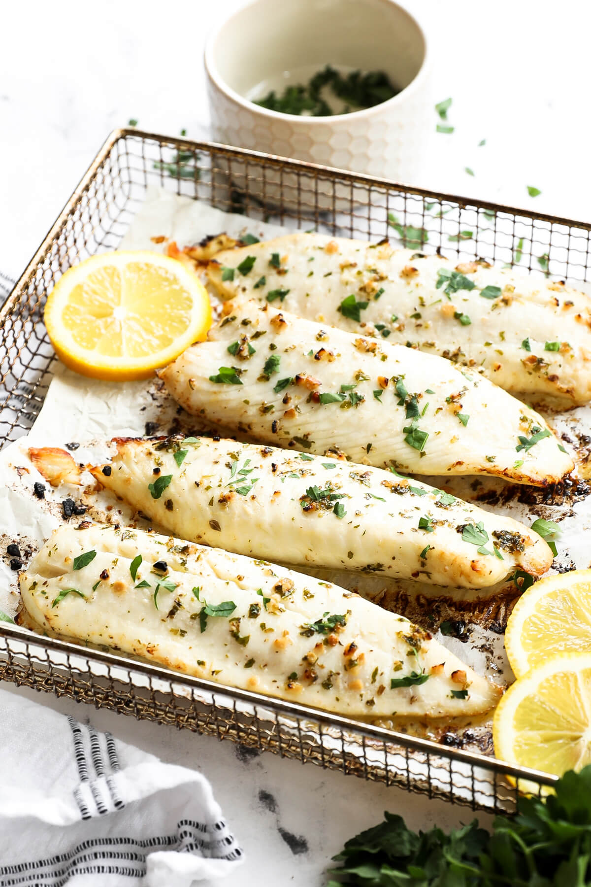 Angled image of air fryer tilapia in cooking basket with lemon slices and parsley garnish.