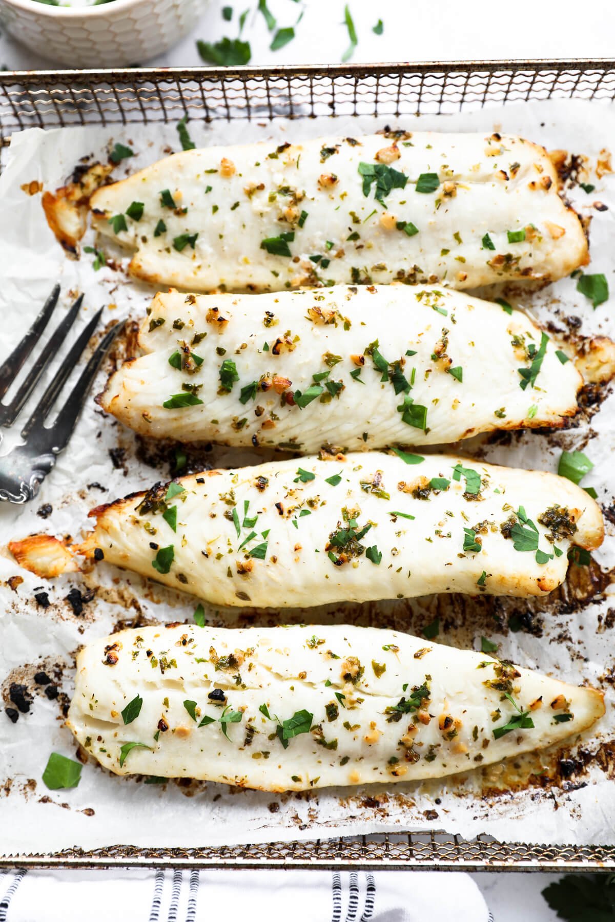 Overhead close up image of four pieces of tilapia lined up in a row. Fresh chopped parsley sprinkled on top.