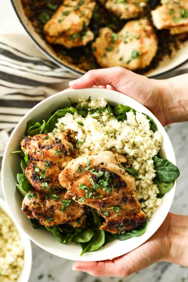 Image of holding a bowl with greens, cauliflower rice and lemongrass chicken with chopped cilantro on top. 