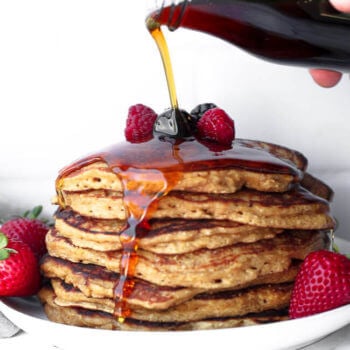 Stack of gluten free pancakes with maple syrup being poured on top and dripping down the side of the stack.