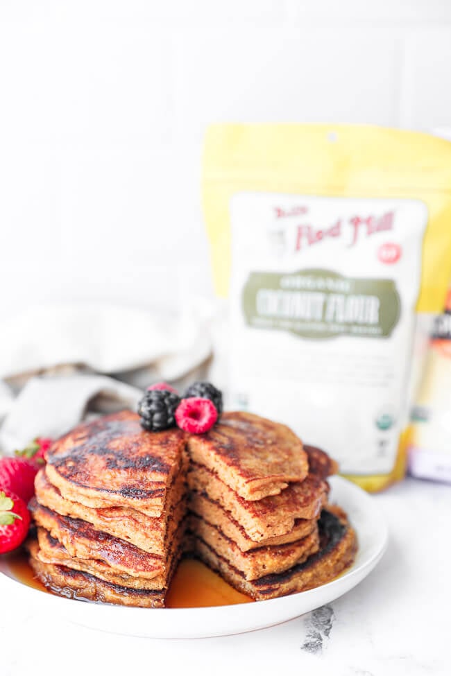 Straight on image of stack of gluten free pancakes with berries on top and a big bite cut out of the stack. 