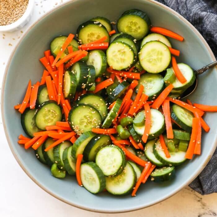 Overhead image of a bowl full of cucumber, carrots and celery with a sesame sauce and sesame seeds. Ingredients are all mixed up.