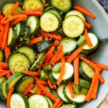 Close up overhead image of a bowl full of cucumber, carrots and celery with a sesame sauce and sesame seeds. Ingredients are all mixed up.