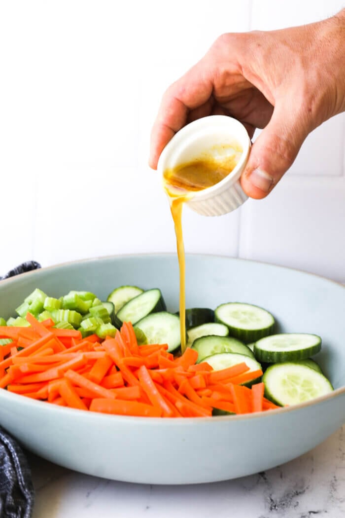 Image of pouring salad dressing/sauce into the bowl of ingredients.