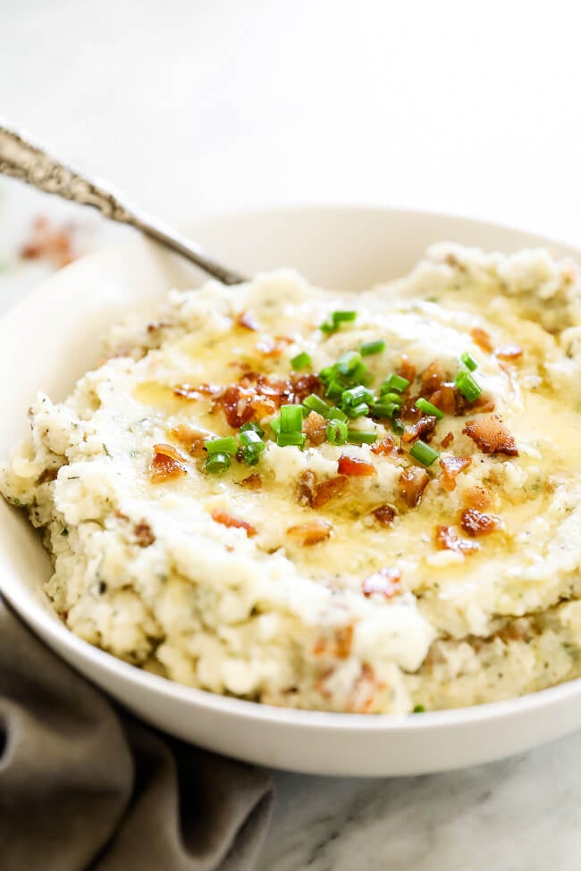 Vertical angled image of loaded mashed cauliflower in a bowl with a serving spoon in it. 