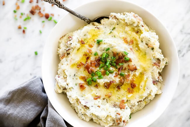 Horizontal overhead image of loaded mashed cauliflower in a bowl with a serving spoon. 