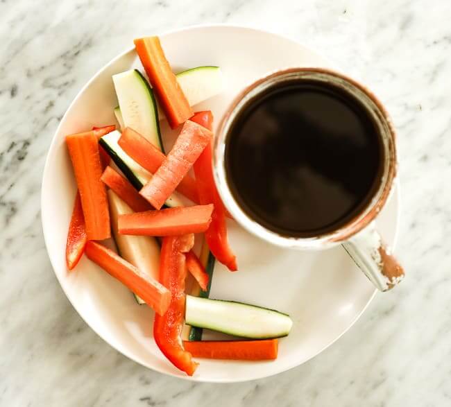 Sliced carrots, bell pepper and zucchini on a plate with a cup of broth