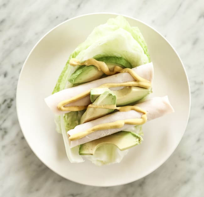 Iceburg lettuce shell topped with lunch meat, avocado and mustard on a plate