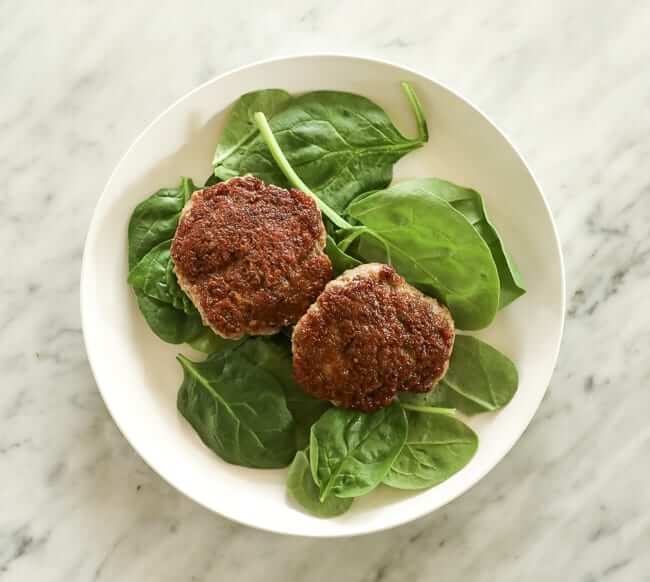 Spinach topped with two sausage patties on a plate
