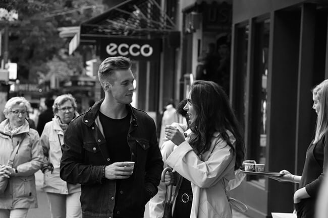 Man and woman on street with cups looking at each other