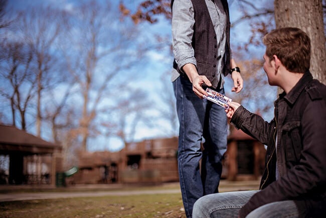 Man handing another man a postcard in a park