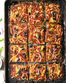 Overhead shot of sheet pan of meat pizza sliced into squares with cheese, olive, bell pepper and red onion topping