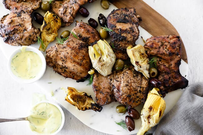 Grilled mediterranean chicken on a  platter with artichoke hearts, olives and sauce overhead shot.