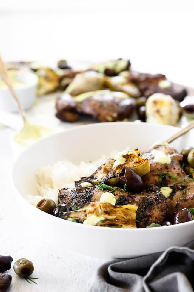 Angle image image of grilled mediterranean chicken in a bowl with rice, artichoke hearts and olives.