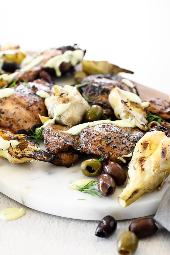 Grilled mediterranean chicken on a  platter with artichoke hearts, olives and sauce close up angle shot.
