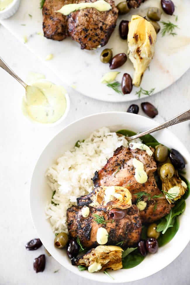 Overhead image of grilled mediterranean chicken in a bowl with rice, artichoke hearts and olives.