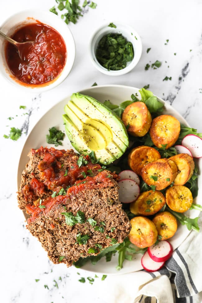 Mexican meatloaf slices on a plate with avocado, greens and sliced plantains