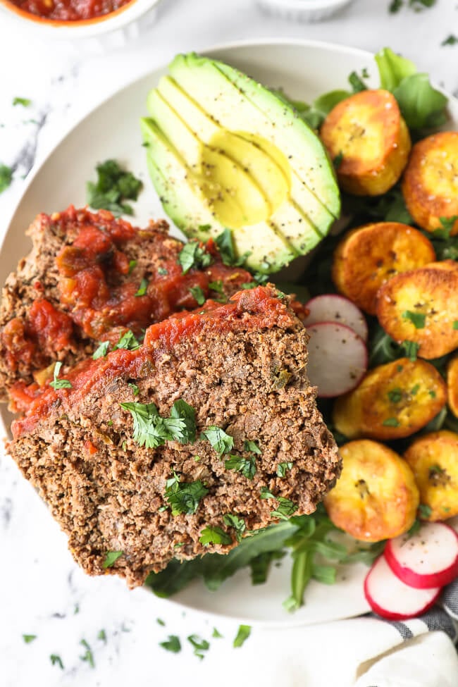 Mexican meatloaf slices on a plate with avocado, greens and sliced plantains close up vertical image