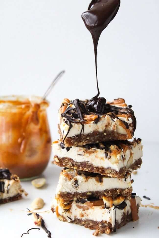 Stack of four no bake snickers cheesecake bars with chocolate drizzle on top