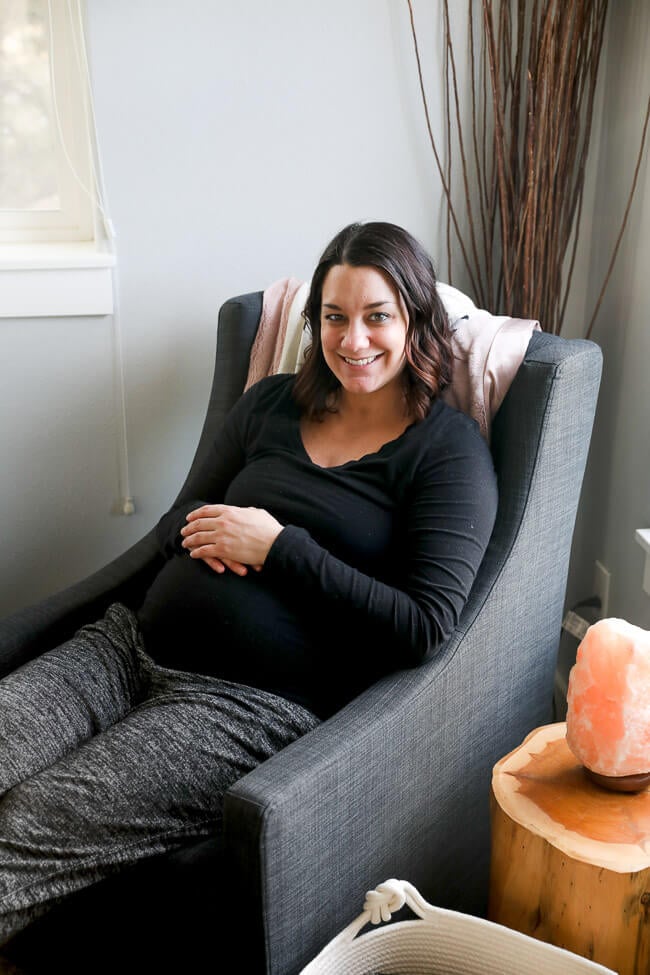 Erica Winn sitting in a rocking chair smiling with hands resting on pregnant belly. 