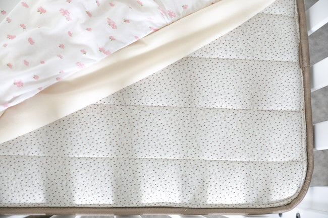 Horizontal overhead image of non-toxic crib mattress with waterproof mattress cover and fitted sheet pulled off the corner of the mattress. 