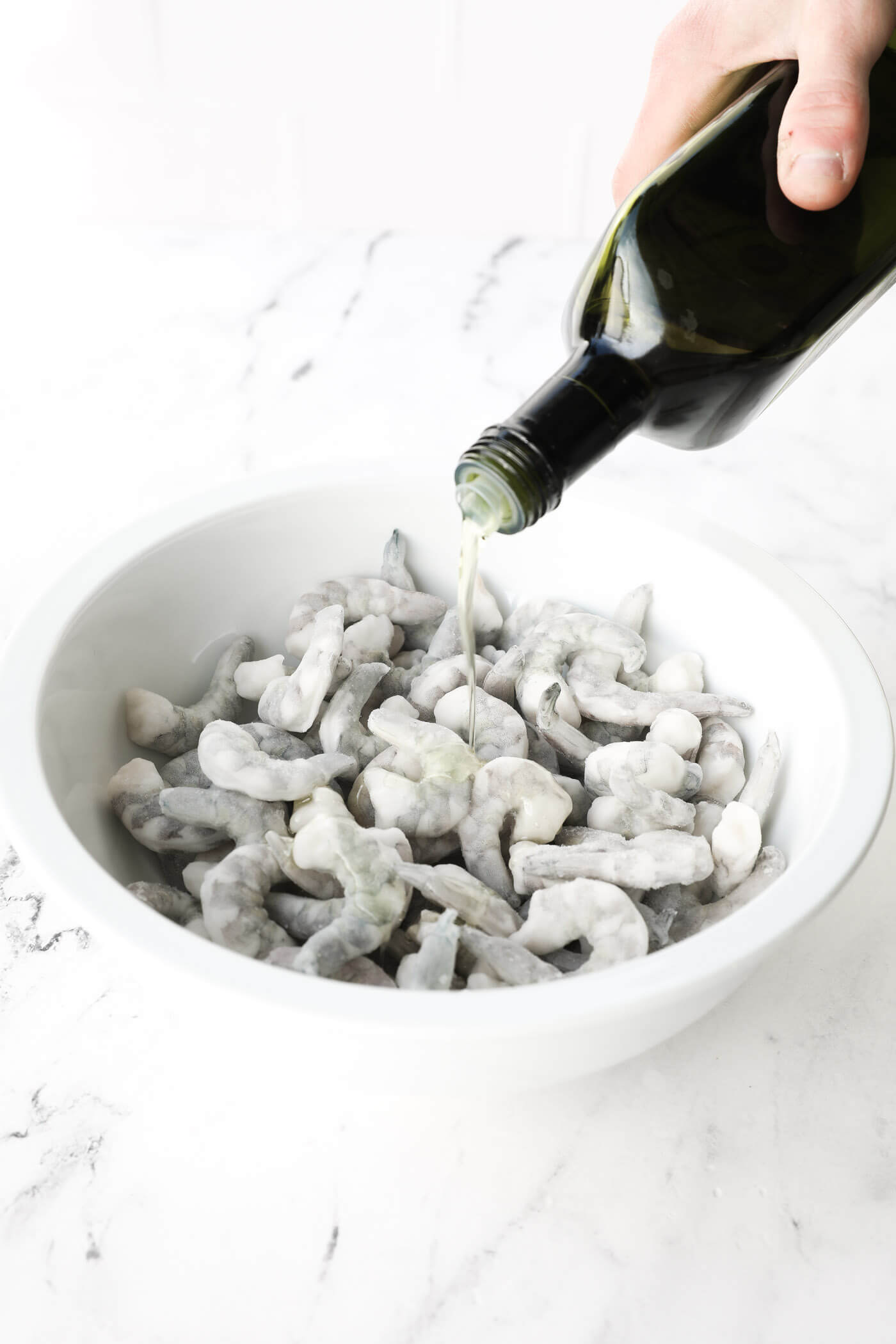 Pouring oil over frozen shrimp in a large bowl.