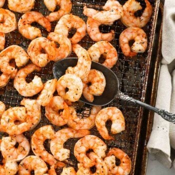Air fryer shrimp after cooking in the air fryer basket with a serving spoon scooping a few pieces up.